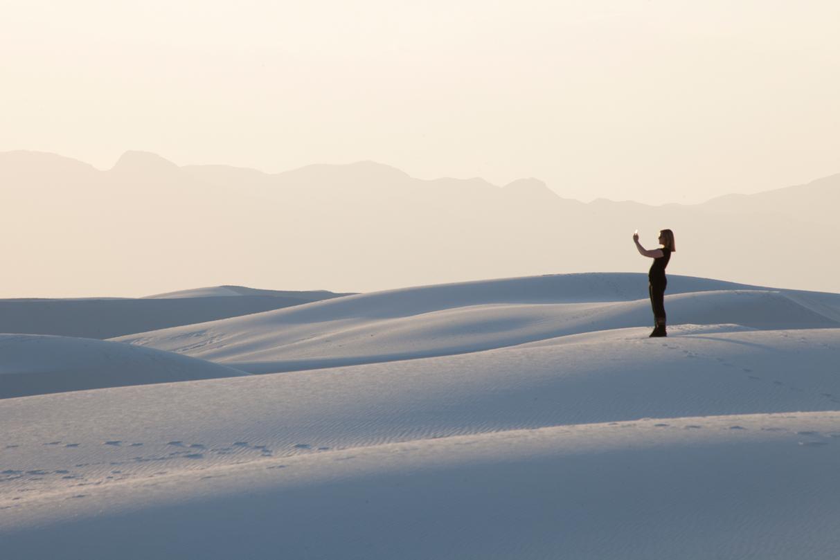 A woman taking a photograph against the white sand and sky