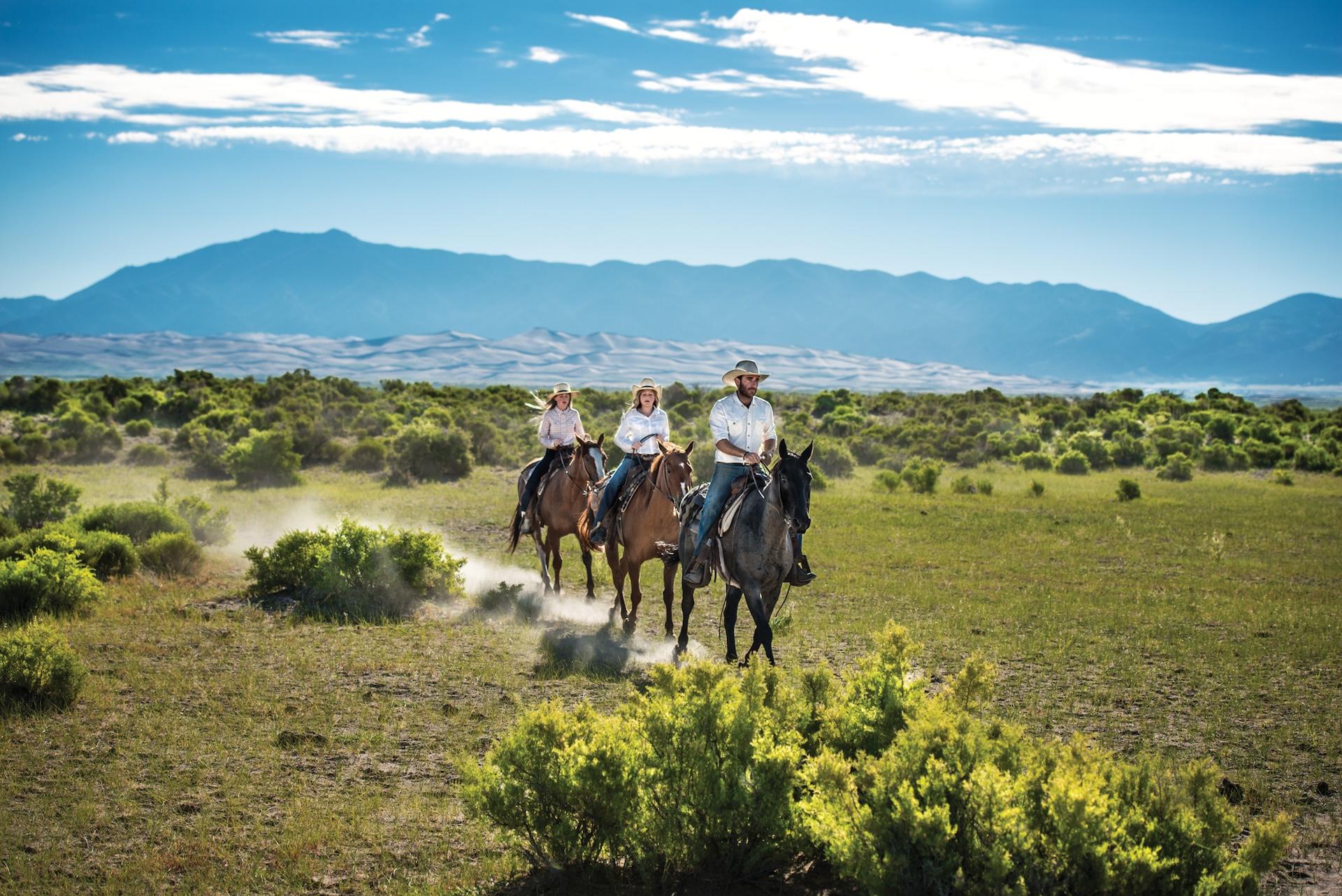 Three riders on horseback with the Great Sand Dunes in the background