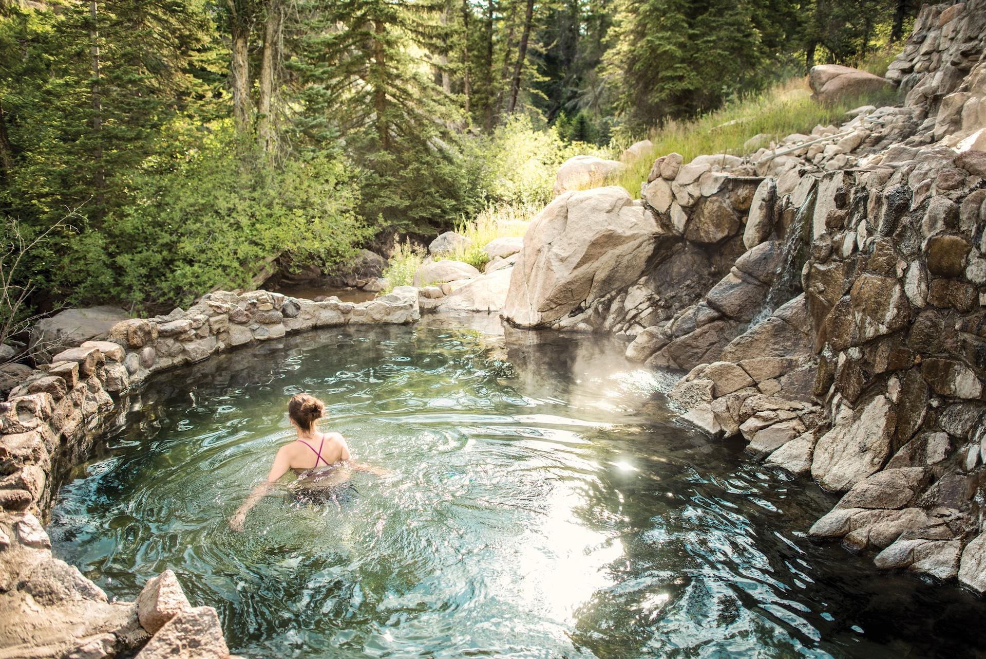 A woman wades in a rock lined spring in the forest