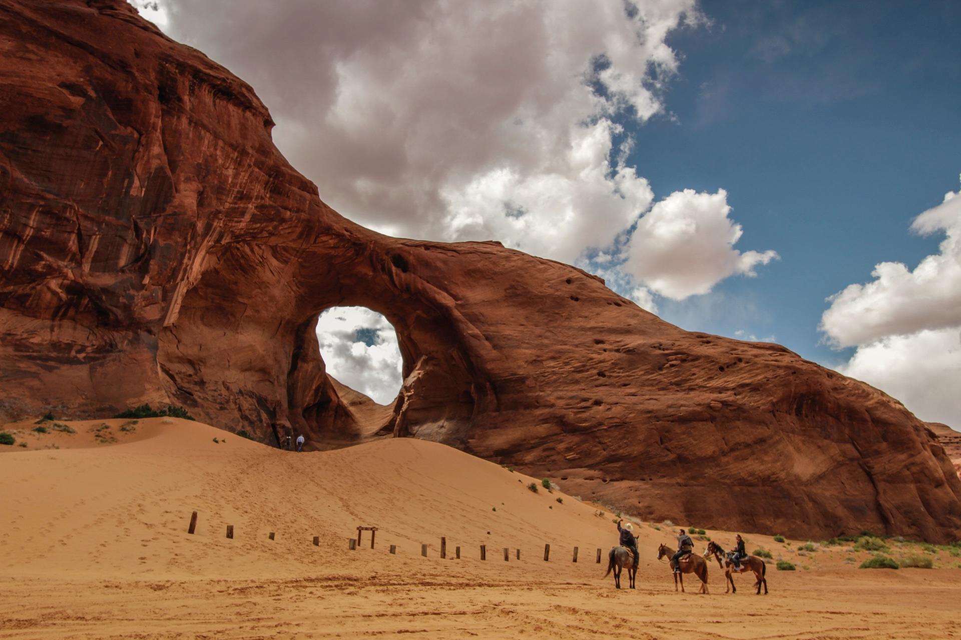 Three riders on horseback pause to look at the arch