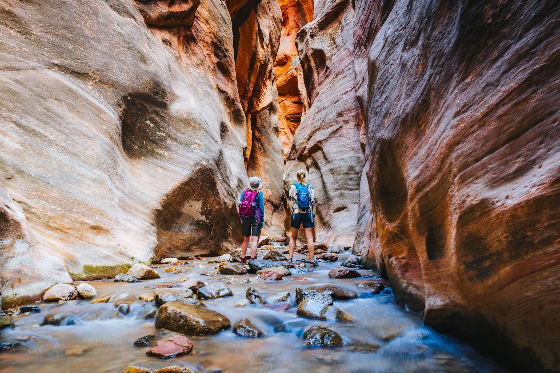 Two hikers going through a narrow slot canyon